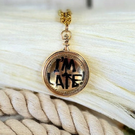 A golden "I'm LATE" pendant rests upon a tangle of creamy threads, its mirrored surface reflecting a hint of adventure, a playful accessory inspired by the whimsy of wonderland.