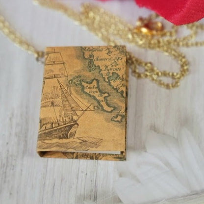 This necklace features a rectangular pendant with a detailed vintage map and ship illustration, evoking adventure, dangling from a textured gold chain.