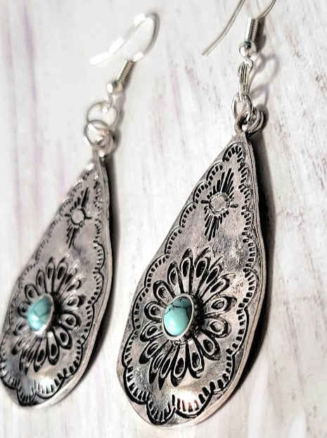 Elegant teardrop-shaped silver earrings with embossed floral patterns and a central turquoise stone, exuding a timeless bohemian charm. A fusion of tradition and trend.