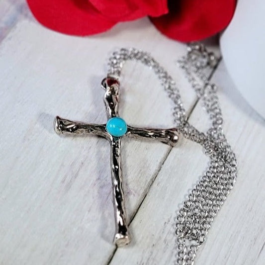 A silver cross necklace with a turquoise stone lies gracefully beside a red rose, casting a delicate shadow, merging spirituality and style.