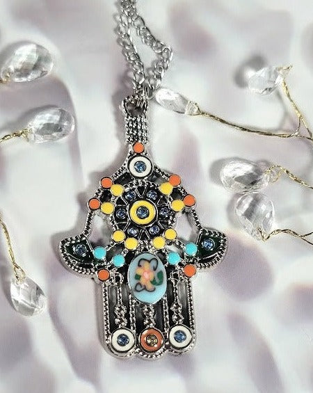 The vivid Hand of Fatima pendant necklace has a colorful mosaic pattern and a playful flower centerpiece, capturing a bohemian spirit with a touch of whimsy.