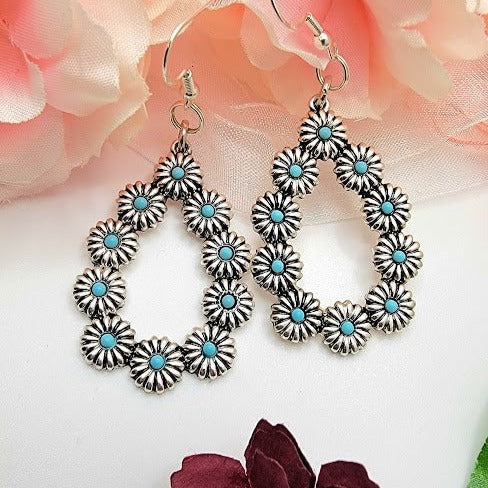 Charming silver-toned earrings with a floral pattern and turquoise-blue centers. Their bohemian design and light-catching petals offer a sophisticated artisanal look.