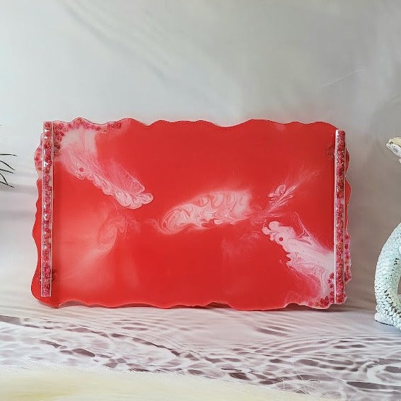 Stunning handcrafted coral-pink resin tray, showcasing captivating white swirls and embellished with glittering edges. Positioned on a rustic whitewashed wooden surface, surrounded by delicate white daisies with bright yellow centers.