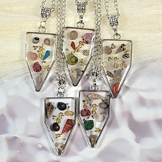 Silver necklaces with hexagonal pendants encasing real miniature seashells in clear resin, displayed on a white floral backdrop.