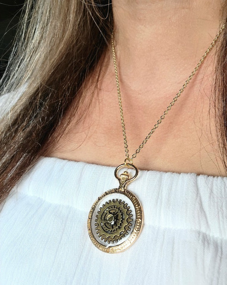 Detailed view of a delicate gold chain leading to an ornate steampunk pendant, worn by a woman with dark hair strands cascading, contrasting against a pristine white blouse.