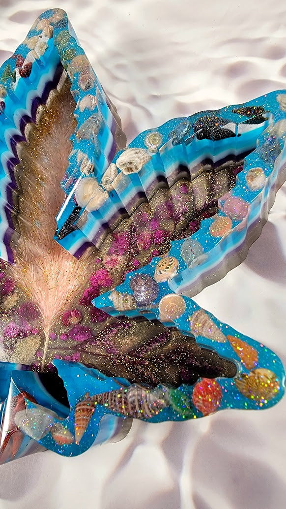 Exquisite close-up of a multicolored resin maple leaf, intricate sea-inspired decorations embedded within, from shells to glistening gems, all converging towards a golden-hued radiant center.