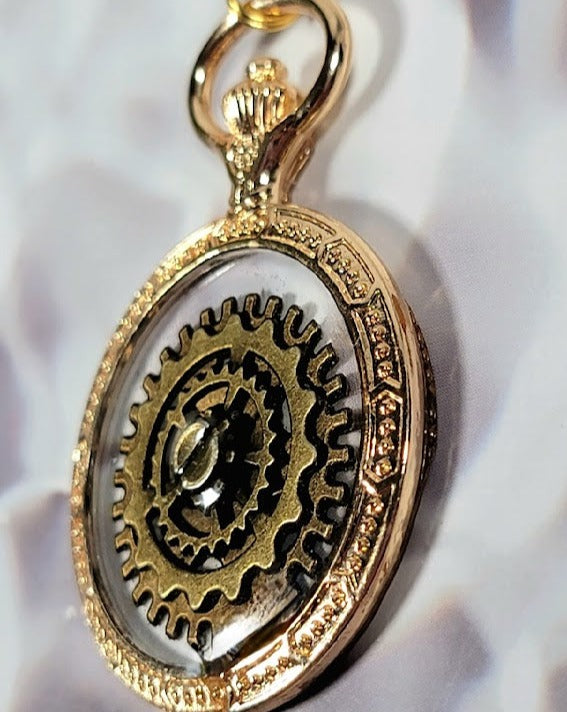 Close-up of a gold steampunk pendant, highlighting intricate gear designs, dangled against a white blouse with subtle pleats, capturing the essence of vintage elegance.