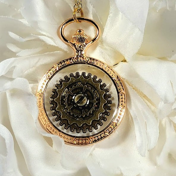 Macro shot of a gold steampunk pendant with delicate outer engravings, a central gear motif, and shimmering details, set against a softly draped white fabric.