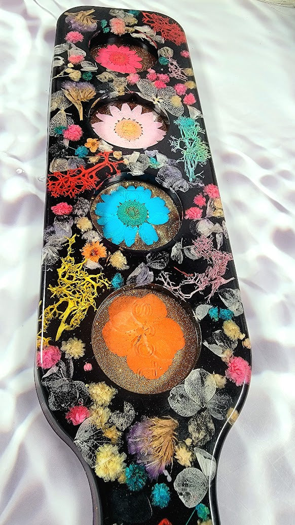 Close-up of a mesmerizing resin masterpiece. Vivid flowers in pink, blue, and orange hues are intricately placed amid detailed plant structures. Each element stands out brilliantly against the stark black canvas, showcasing the artist's dedication.