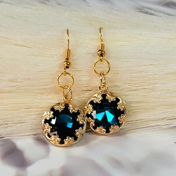 These earrings feature a dazzling blue crystal centerpiece framed by intricate gold detailing, creating a captivating and luxurious piece of jewelry.