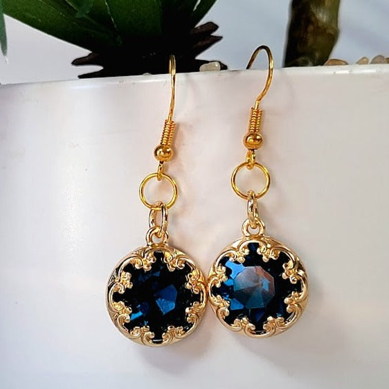 These earrings feature a dazzling blue crystal centerpiece framed by intricate gold detailing, creating a captivating and luxurious piece of jewelry.