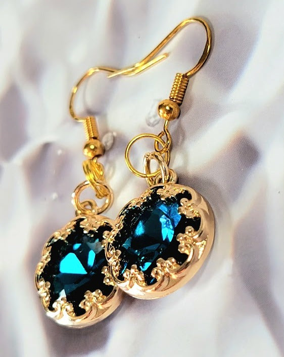 Opulent gold earrings with a captivating deep blue crystal, encircled by delicate golden swirls, reflecting a refined and luxurious aesthetic.