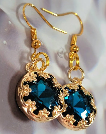 Gold earrings with a stunning blue crystal, intricately designed for an elegant finish, showcased against a gentle and dreamy background.