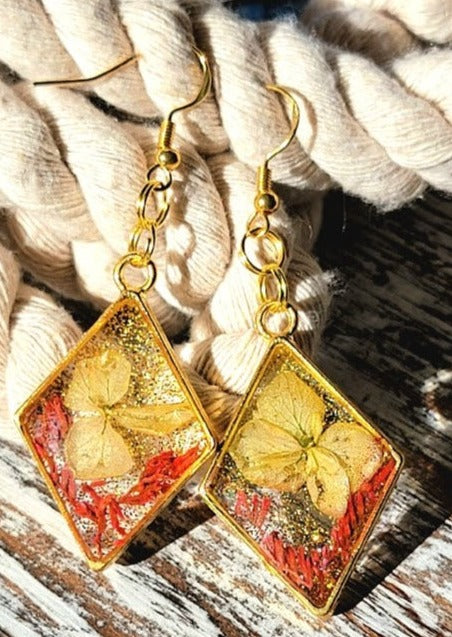 Gold-toned diamond-shaped earrings with embedded autumn leaves and glitter, a perfect accessory to add sparkle and warmth to any fall wardrobe.