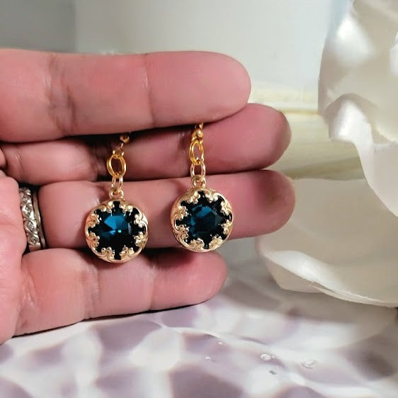 Elegant gold earrings held in hand, featuring captivating dark blue crystals set in an ornate pattern, melding vintage glamour with modern sparkle.