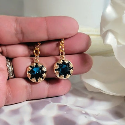 Elegant gold earrings held in hand, featuring captivating dark blue crystals set in an ornate pattern, melding vintage glamour with modern sparkle.