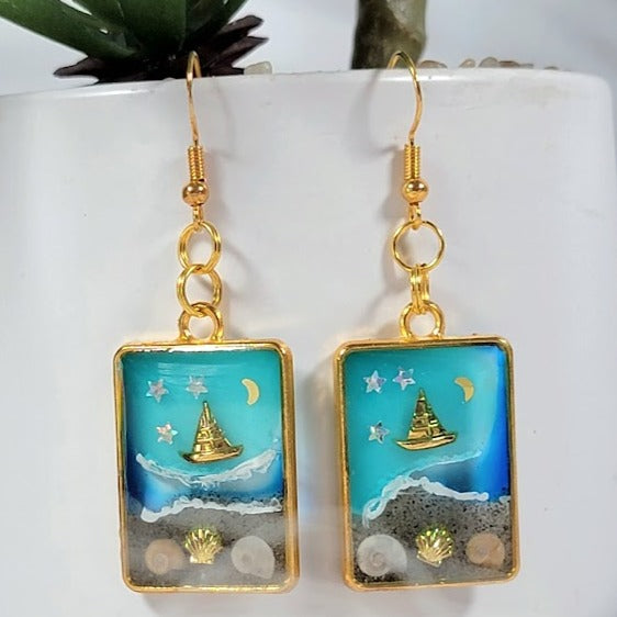 Souvenirs de plage dans un cadre doré, boucles d’oreilles de scène côtière de nuit étoilée, voilier doré sur les eaux bleues célestes, pendentif en résine océanique artisanale