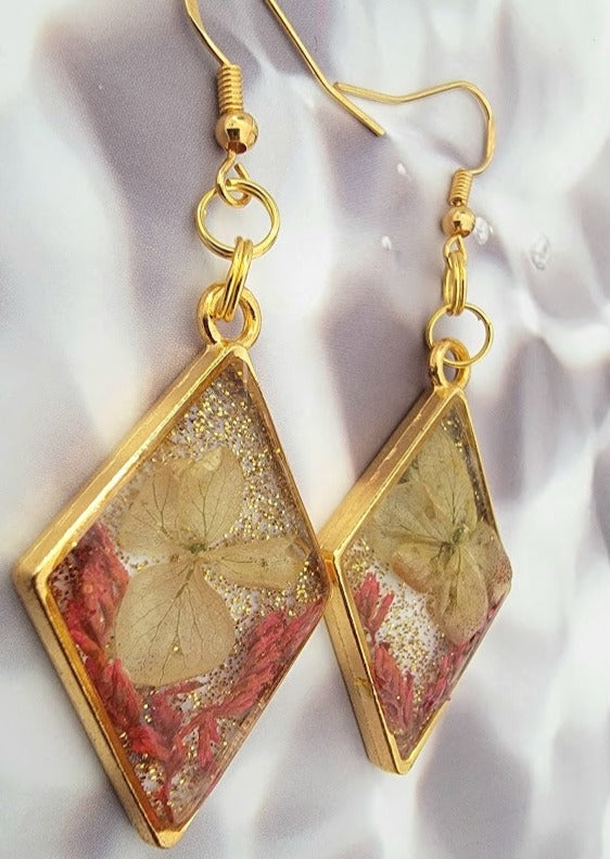 Captured within sleek geometric resin, these floral earrings present a tapestry of nature's delicate work, framed in a lustrous golden border. They're a symphony of floral elegance and contemporary style.