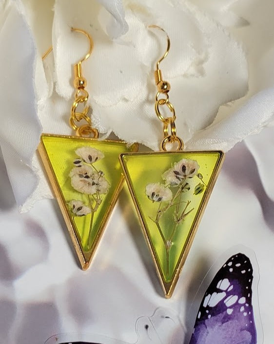 Bright yellow resin triangle earrings with white floral inlays dangle above a whimsical butterfly, merging nature's beauty with handcrafted artistry.