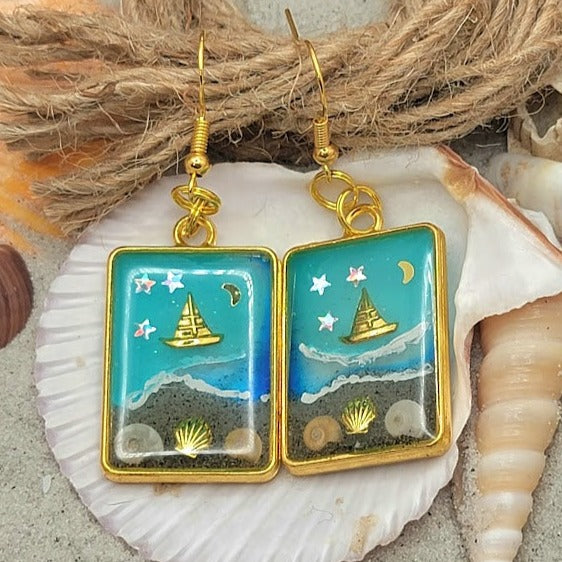 Souvenirs de plage dans un cadre doré, boucles d’oreilles de scène côtière de nuit étoilée, voilier doré sur les eaux bleues célestes, pendentif en résine océanique artisanale