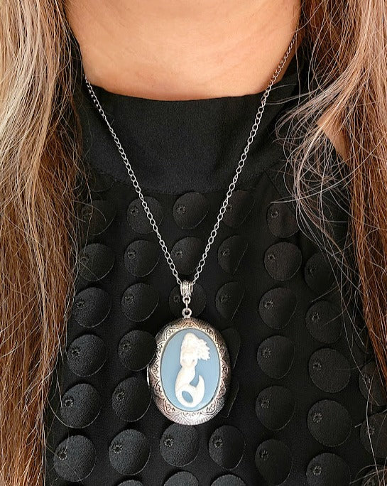 A beautifully handcrafted silver mermaid cameo pendant necklace contrasts strikingly against a black textured blouse, embodying a sophisticated and enchanting oceanic theme.