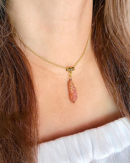 A slender gold chain holds a crystalline pink pendant, its facets catching the light and adding a touch of natural elegance to a simple white neckline.