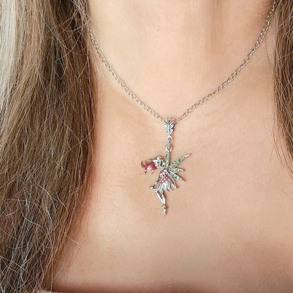 A delicate silver fairy necklace with a pink and green sparkle design, worn on a slender chain, rests just above the collarbone against a backdrop of long, wavy hair and a soft white neckline.