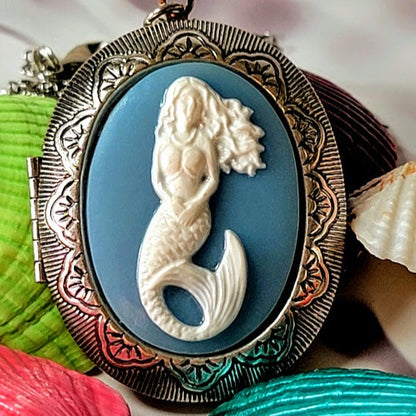 Ornate silver-framed mermaid cameo pendant featuring a detailed carving on a serene blue background, capturing the mythical grace of ocean lore.