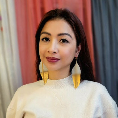 Confident and stylish, a woman in a white top radiates as she showcases bold, gold leaf earrings that catch the light with modern flair.