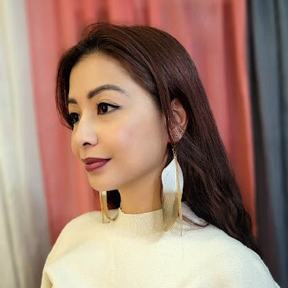 A woman with a poised expression models sleek gold leaf earrings, their elegant simplicity complementing her sophisticated style.