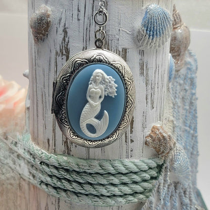 Silver necklace with a mermaid cameo pendant, artistically draped over a rustic white post adorned with rope and seashells, evoking a maritime aesthetic.