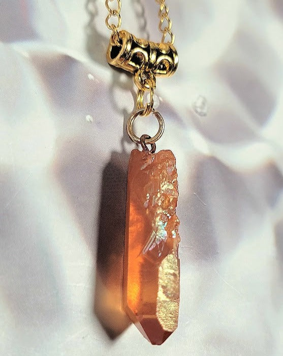 A golden chain with a raw pinkish-brown crystal pendant captures the light, showcasing its natural, rugged beauty against a silky background.