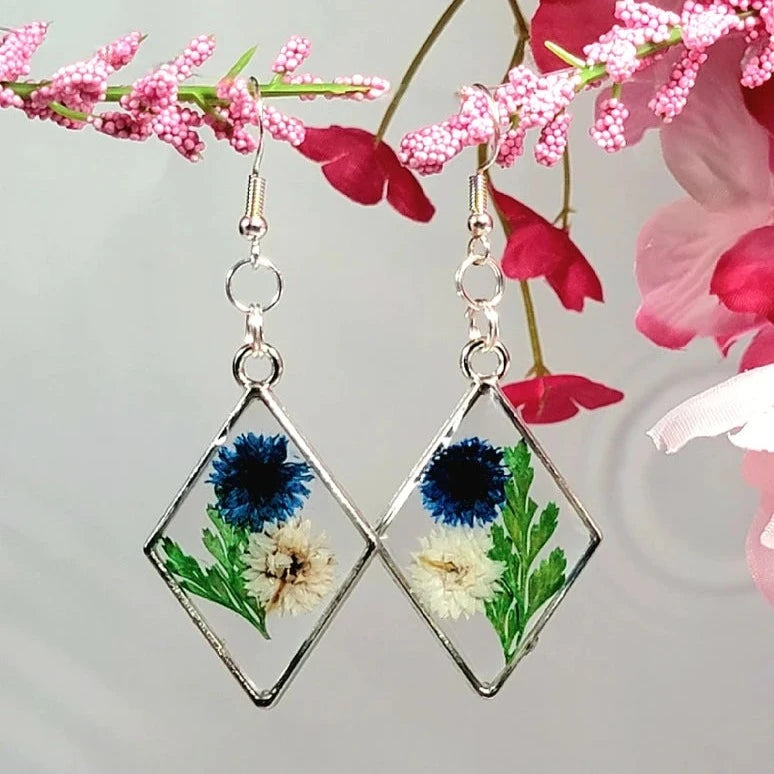 Pendientes de clavel azul y blanco, arte floral contemporáneo, follaje verde exuberante, colgante prensado naturalmente, primavera atemporal