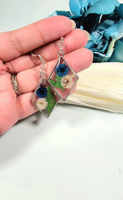 Pendientes de clavel azul y blanco, arte floral contemporáneo, follaje verde exuberante, colgante prensado naturalmente, primavera atemporal