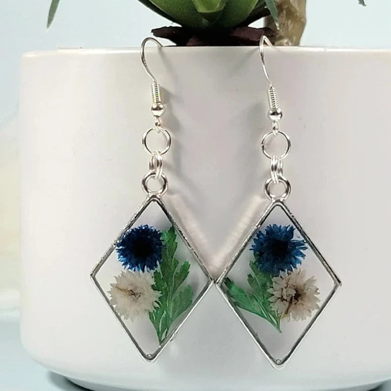 Pendientes de clavel azul y blanco, arte floral contemporáneo, follaje verde exuberante, colgante prensado naturalmente, primavera atemporal