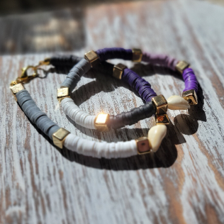 Set of two heishi bead bracelets, one showcasing black and white tones with purple accents, the other inverting the colors, both featuring gold spacers and a statement cowrie shell.