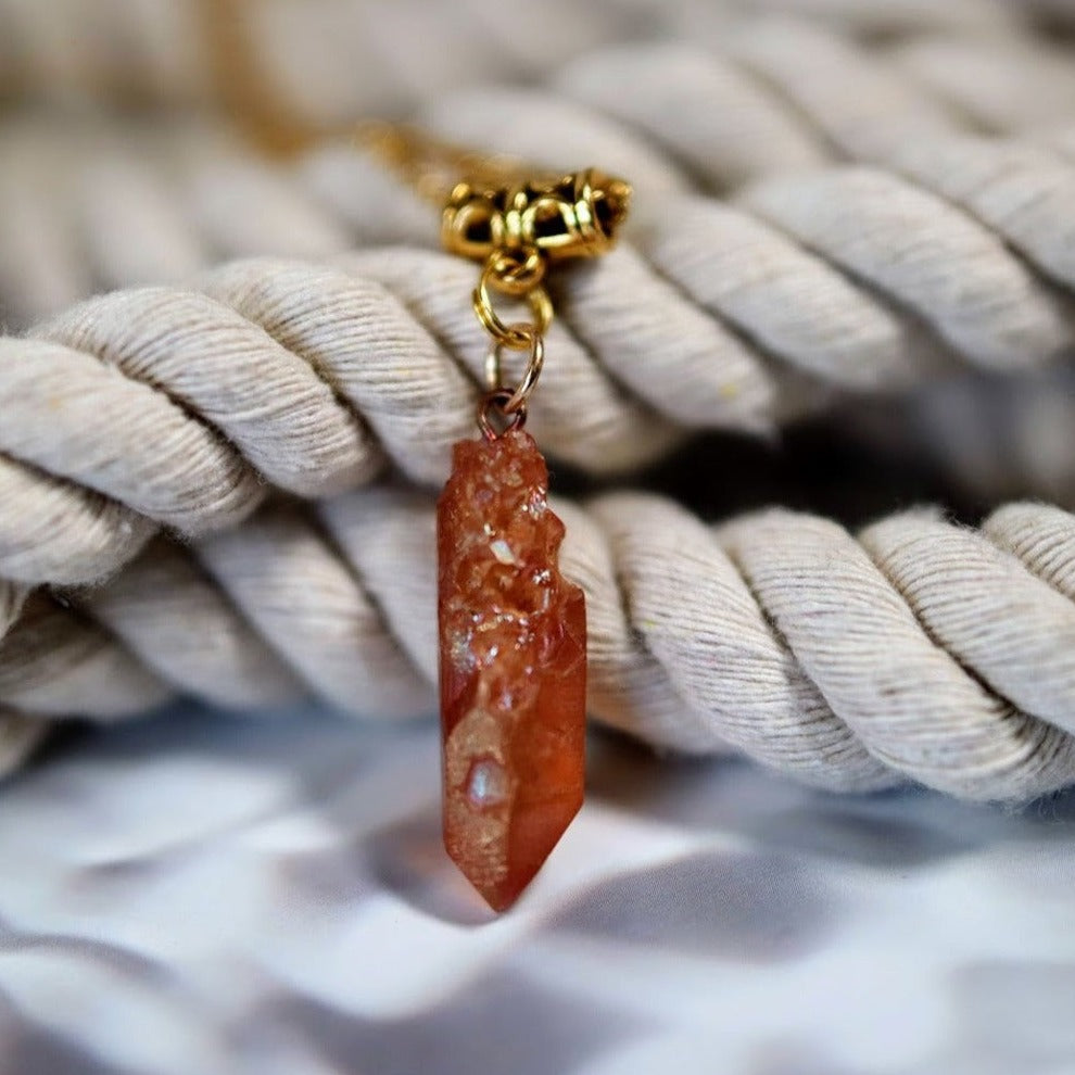 A rugged pink crystal pendant hangs from a golden clasp, cradled by a thick white cotton rope, creating a striking contrast with its raw beauty.