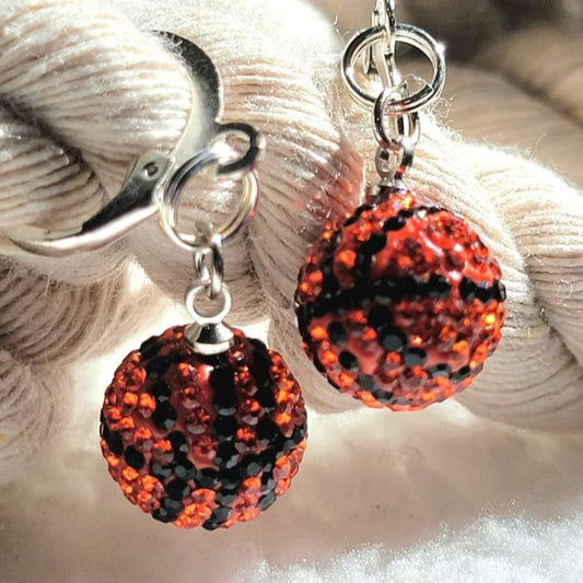 Fiery and captivating, these earrings present two dazzling spheres adorned with shimmering red and black crystals. They hang gracefully from sleek silver clasps, resting against a plush, white, background. 