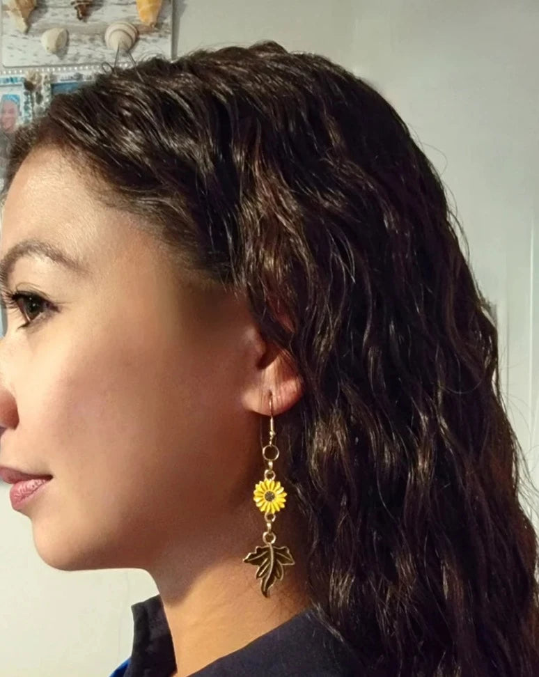 A side profile of a woman showcases sunflower and maple leaf earrings, where the vivid autumnal colors add a playful yet elegant charm to her look.