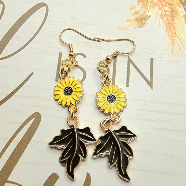 Golden earrings featuring sunflowers and autumn leaves dangle against a backdrop of cursive script, capturing a cheerful essence with a hint of nostalgia.