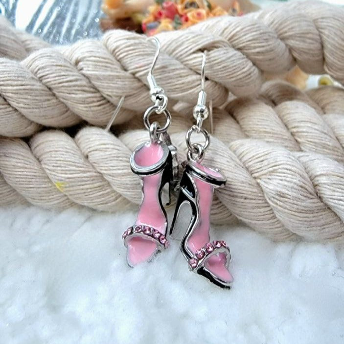 Elegant pink high-heel shoe earrings with shimmering rhinestone details, showcased against soft coiled ropes.