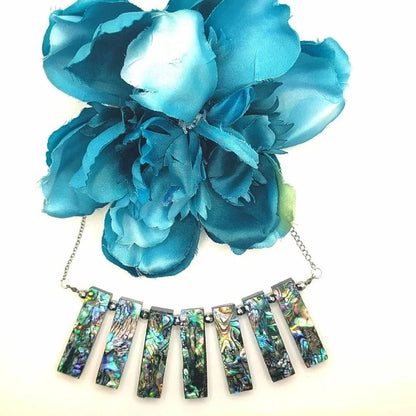 Handcrafted necklace with vibrant blue flower and abalone shell pendants in iridescent hues on a silver chain, exuding elegance and craftsmanship.