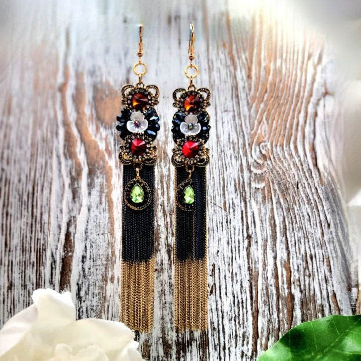 Striking dangle earrings with black and gold beadwork, adorned with colorful rhinestones and floral motifs, cascading into elegant tassels, embodying a blend of classic glamour and modern sophistication.