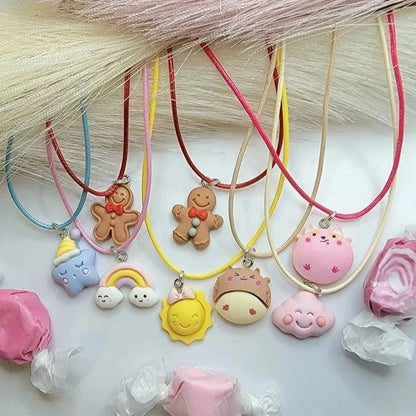 An irresistible collection of pastel-hued necklaces, each with a whimsical charm, is laid out beneath a silky cascade of pale pink & cream tassels. The charms include playful gingerbread men, smiling suns, pastel rainbows, fluffy clouds, and more.