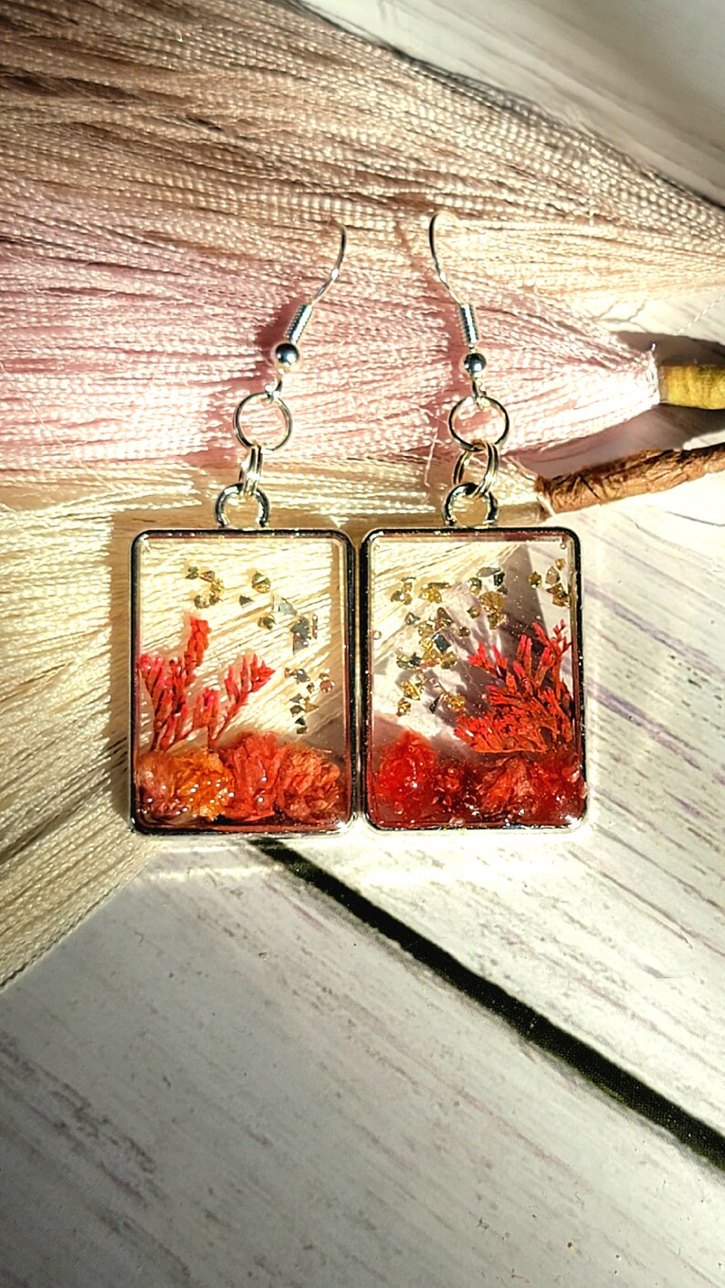 Accessoires nature avant-gardistes, petits boutons floraux dans une lunette carrée argentée, boucles d’oreilles artisanales inspirées de la nature, botanique pêche et orange