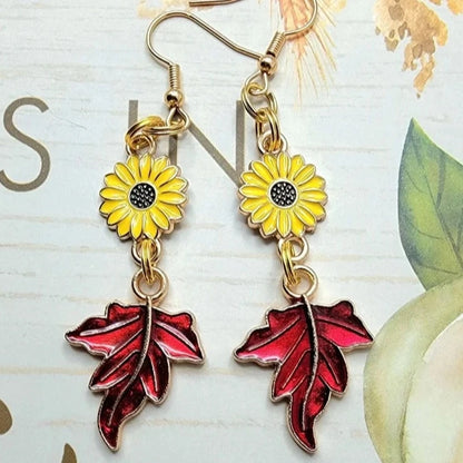 Vibrant yellow sunflower earrings with glossy red maple leaf pendants dangle elegantly against a backdrop of vintage florals, summoning the essence of autumn. 