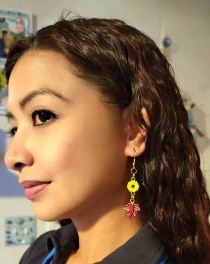 A side profile of a woman with sunflower and maple leaf earrings dangling gracefully. The autumn-themed jewelry pops against her blue top, adding a playful and seasonal touch. 