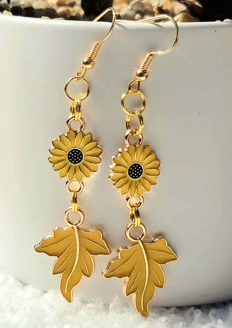 These charming earrings showcase vibrant yellow sunflowers linked to delicate maple leaves, capturing the essence of a golden autumn day.